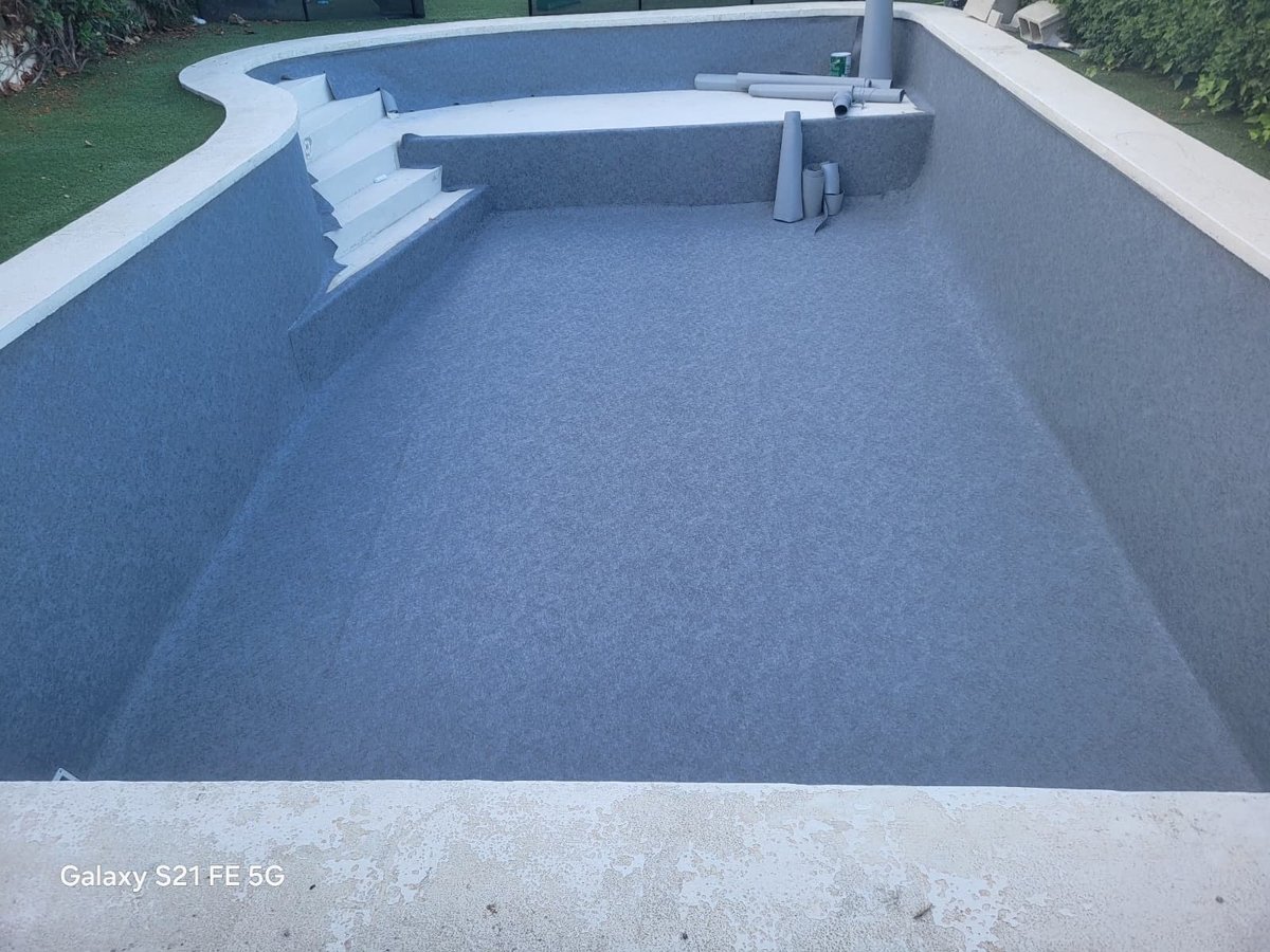Empty concrete swimming pool with blue interior coating and white coping, viewed from above during construction or renovation