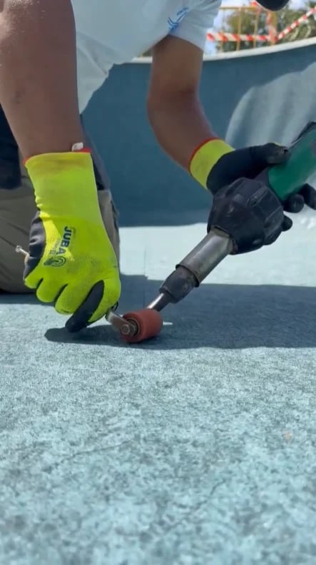 Worker in neon yellow gloves using pneumatic tool on roofing material during installation