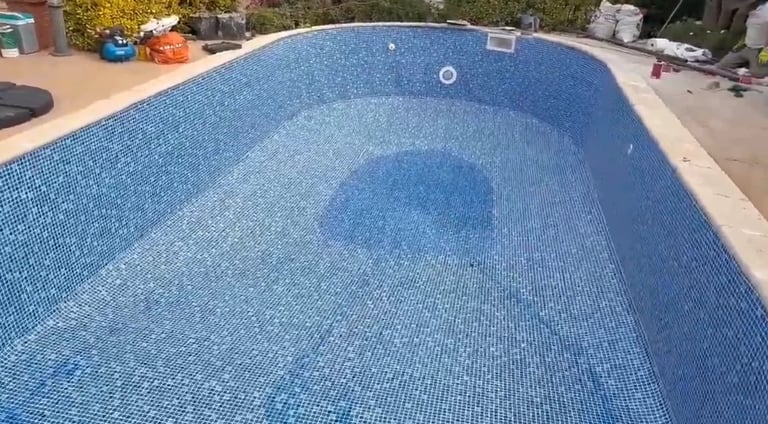 Empty in-ground swimming pool with blue tiled interior and concrete deck surrounded by landscaping