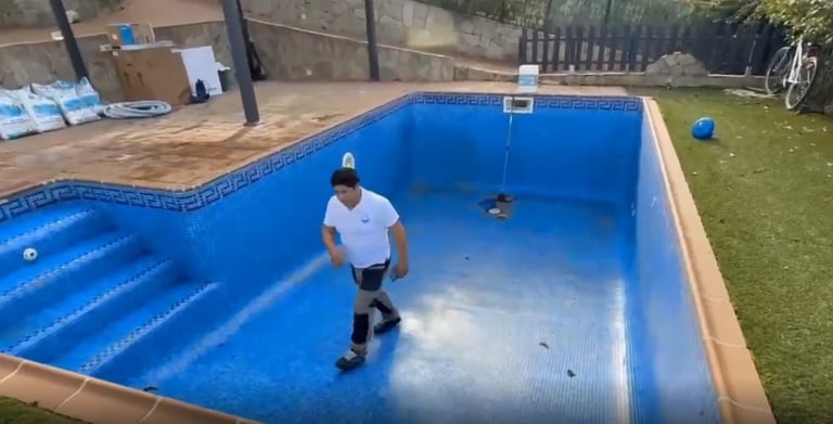 Man in white shirt standing in empty blue swimming pool during maintenance or cleaning